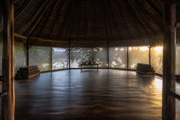 Empty maloca at dawn after an ayahuasca ceremony, mats rolled and candle extinguished